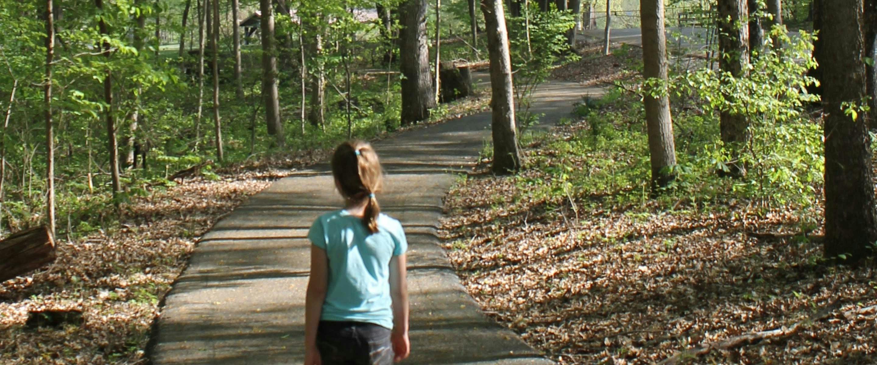 girl walking on paved nature trail to tree forrest canopy area in shade