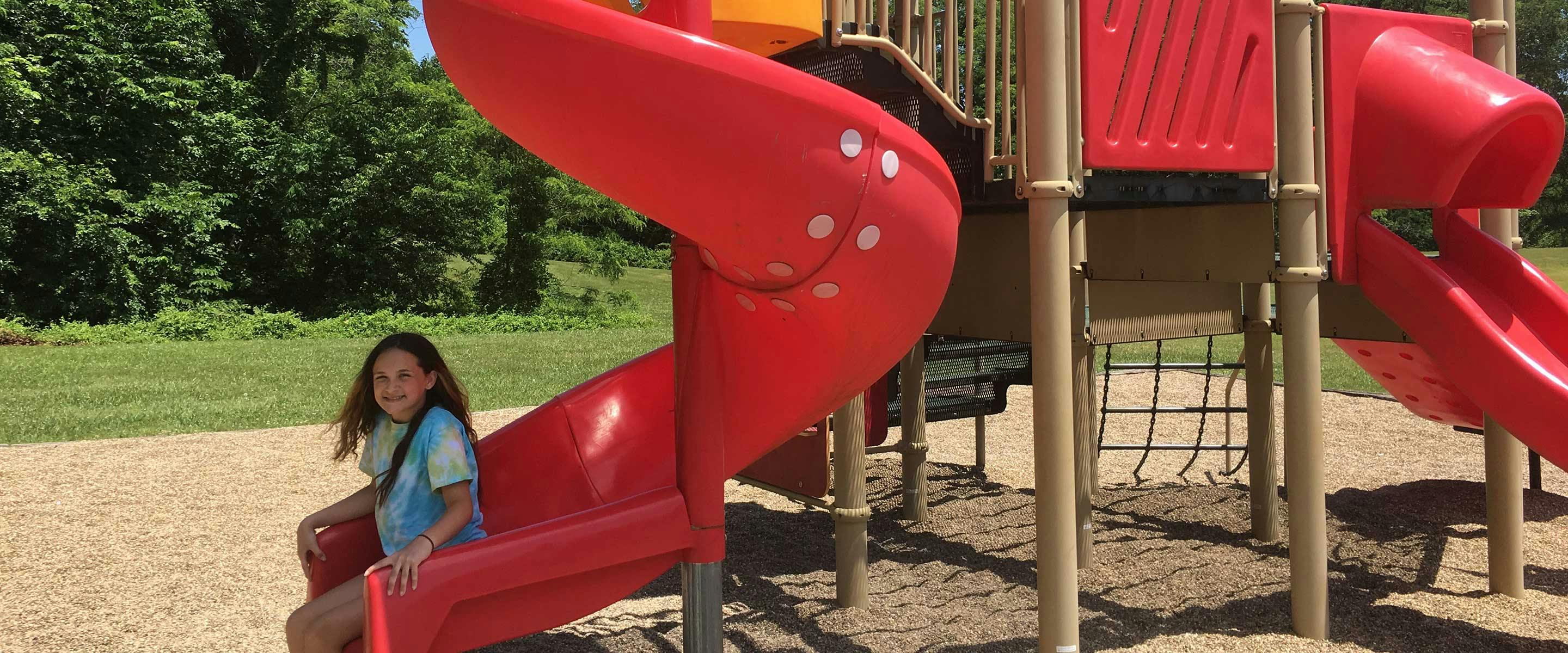 girl sliding down red slide at harrison county parks playground